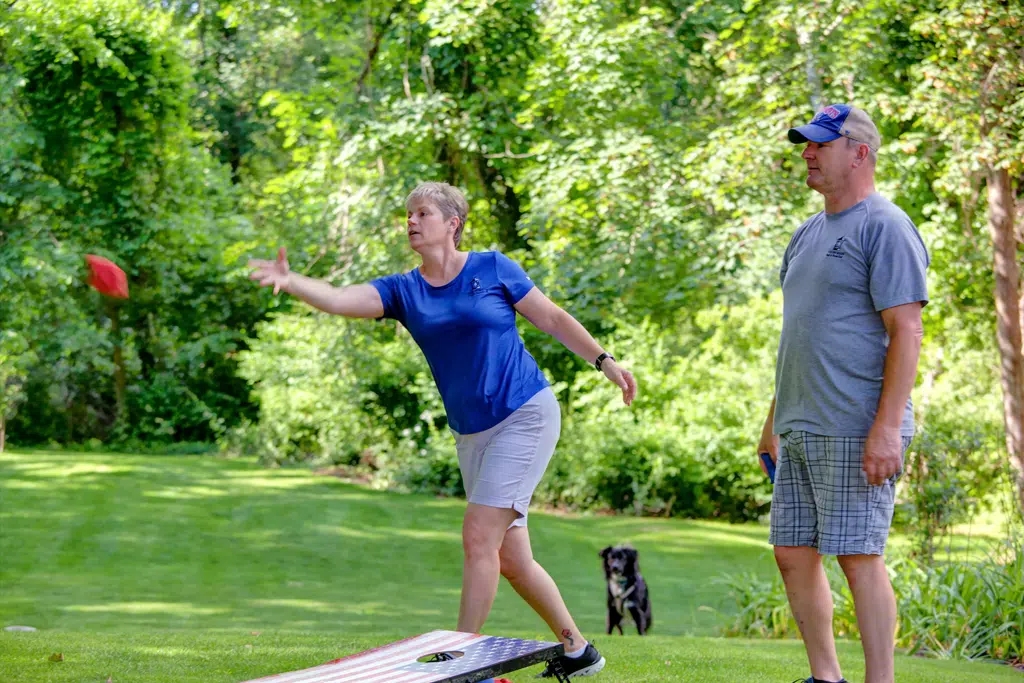 Woman in blue shirt and khaki shorts with man in grey shirt and grey checked shorts playing cornhole