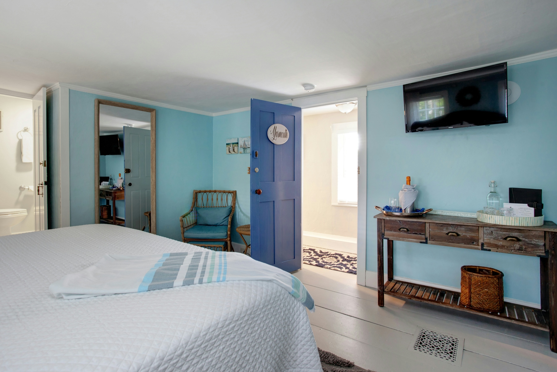 View of wall opposite bed with console table, wall-mounted flat-screen TV,  and doorway leading to hall