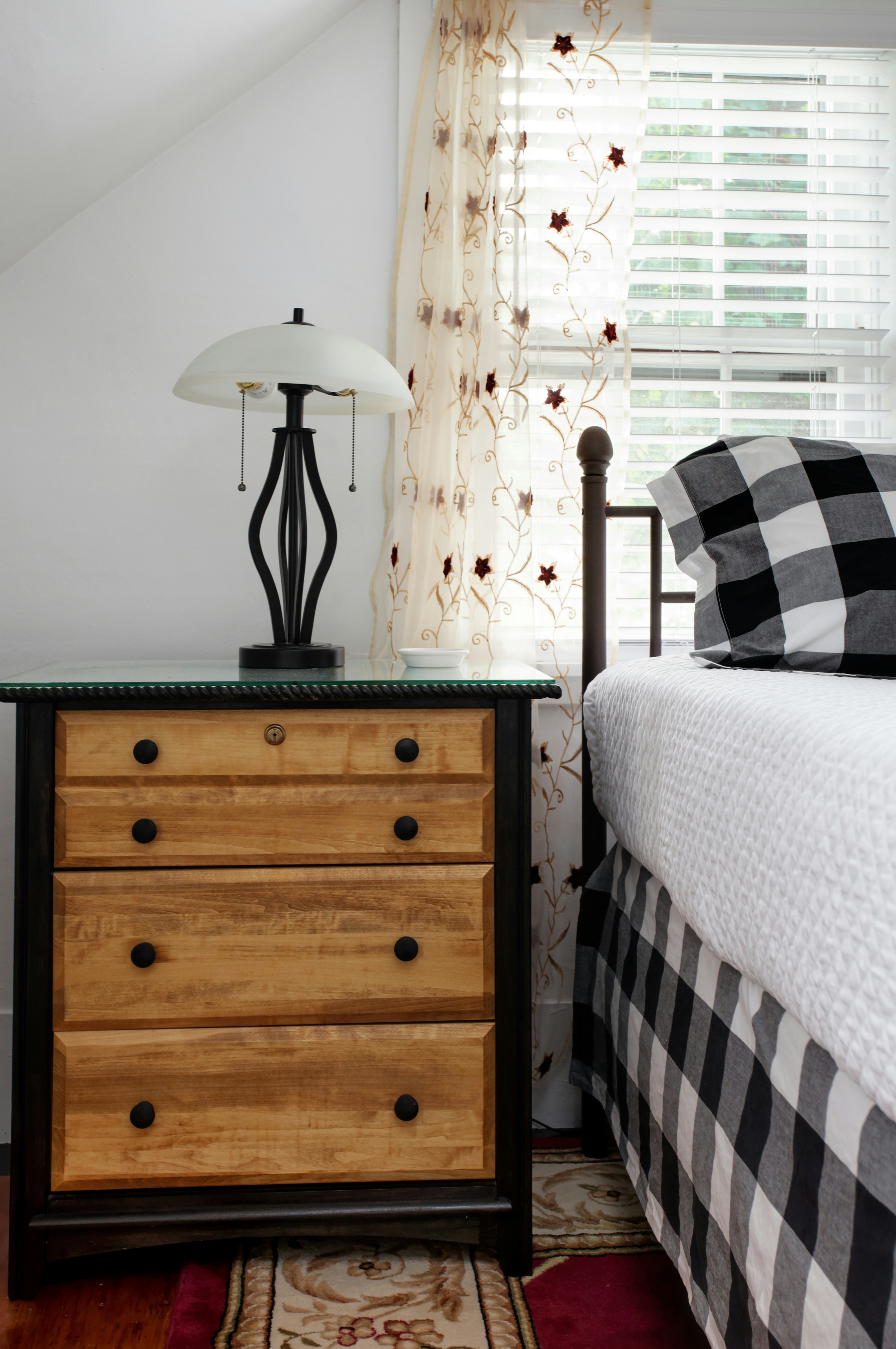 Natural wood and black painted nightstand with lamp beside bed