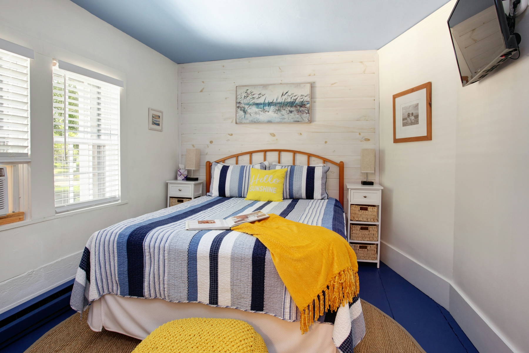 Bed topped with blue and white striped bedding, yellow throw pillow and yellow blanket, wooden nightstands with basket drawers