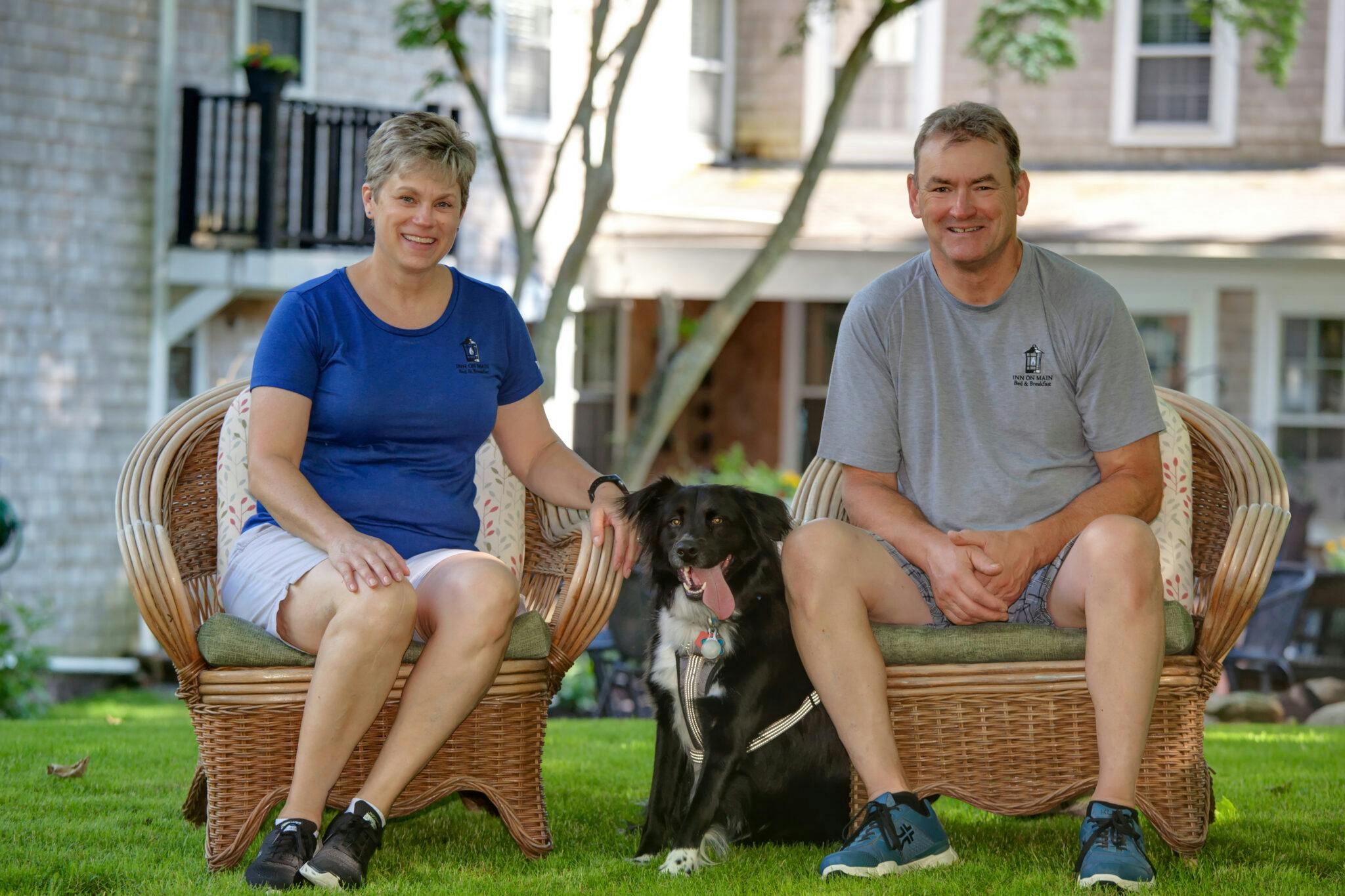 Innkeepers sitting in yard on wicker chairs with black dog sitting between them