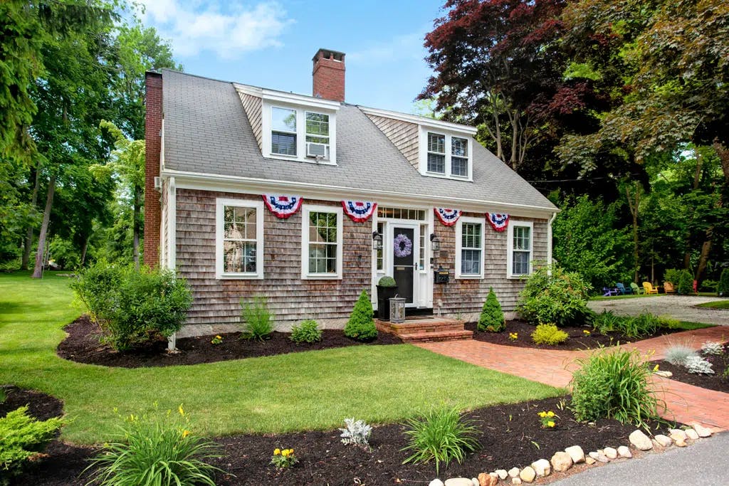 Front of inn with grey clapboard and dormers with fourth of july bunting displays