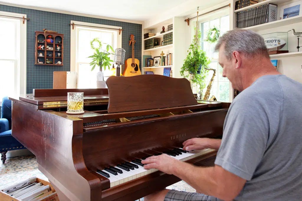 Man in grey shirt sitting at brown yamaha grand piano playing