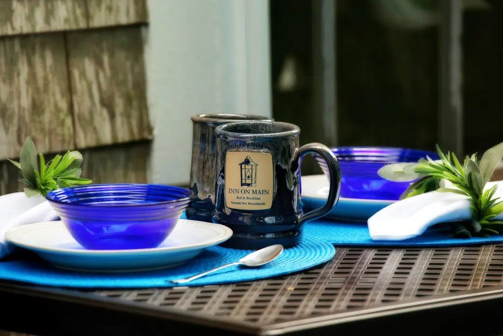 Blue plates and blue placemats on black metal table with custom inn coffee mugs