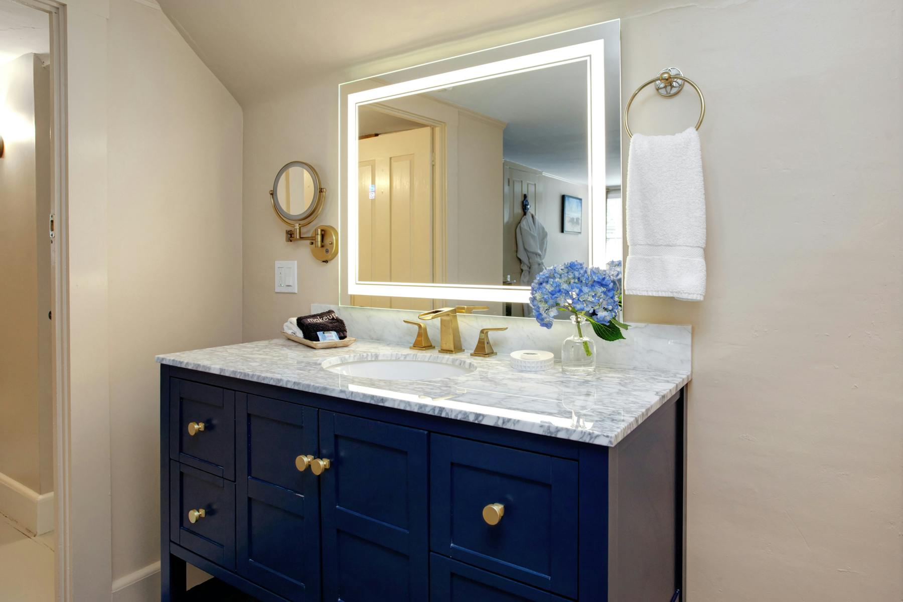 Wooden navy colored bathroom vanity with white top and gold fixtures, mirror above