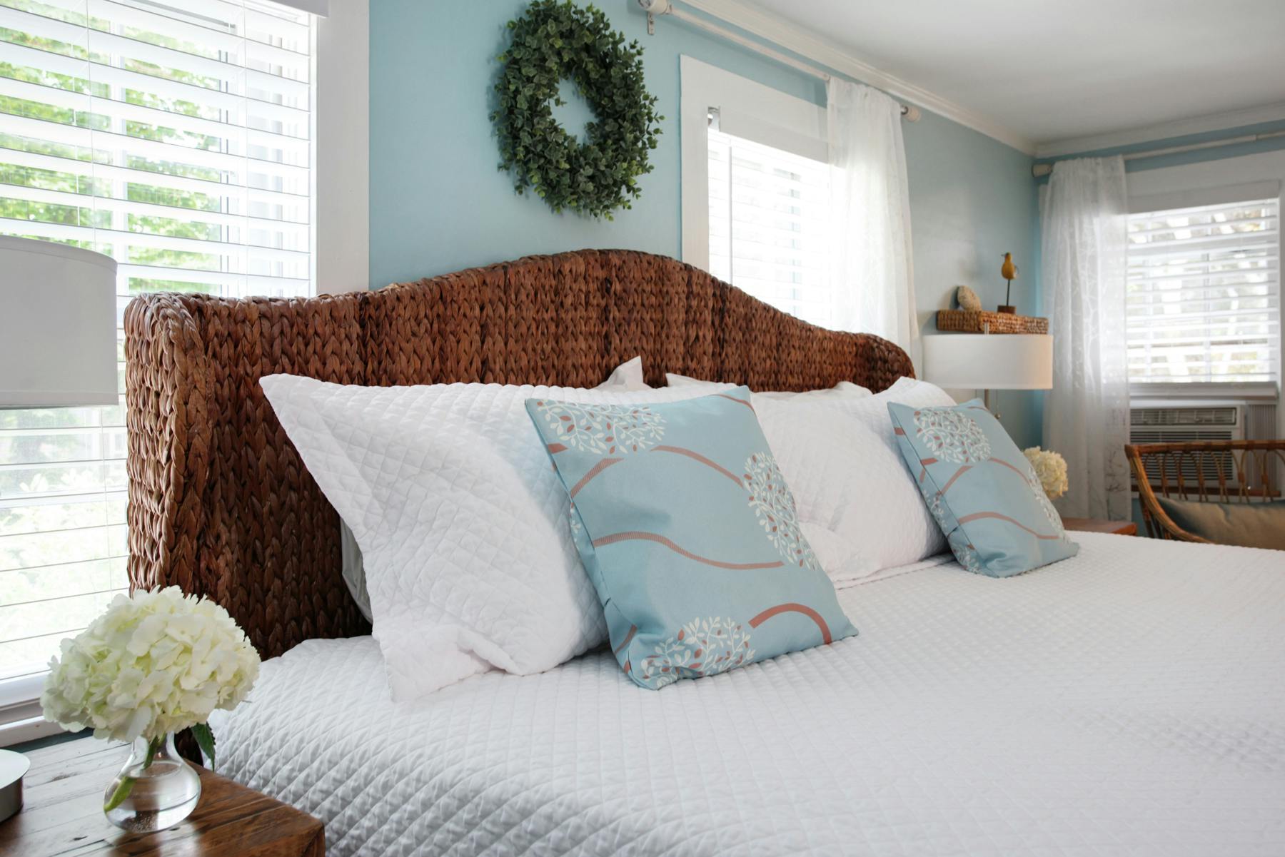 Close up of king bed with rattan headboard, white quilted bedcover and decorative throw pillows