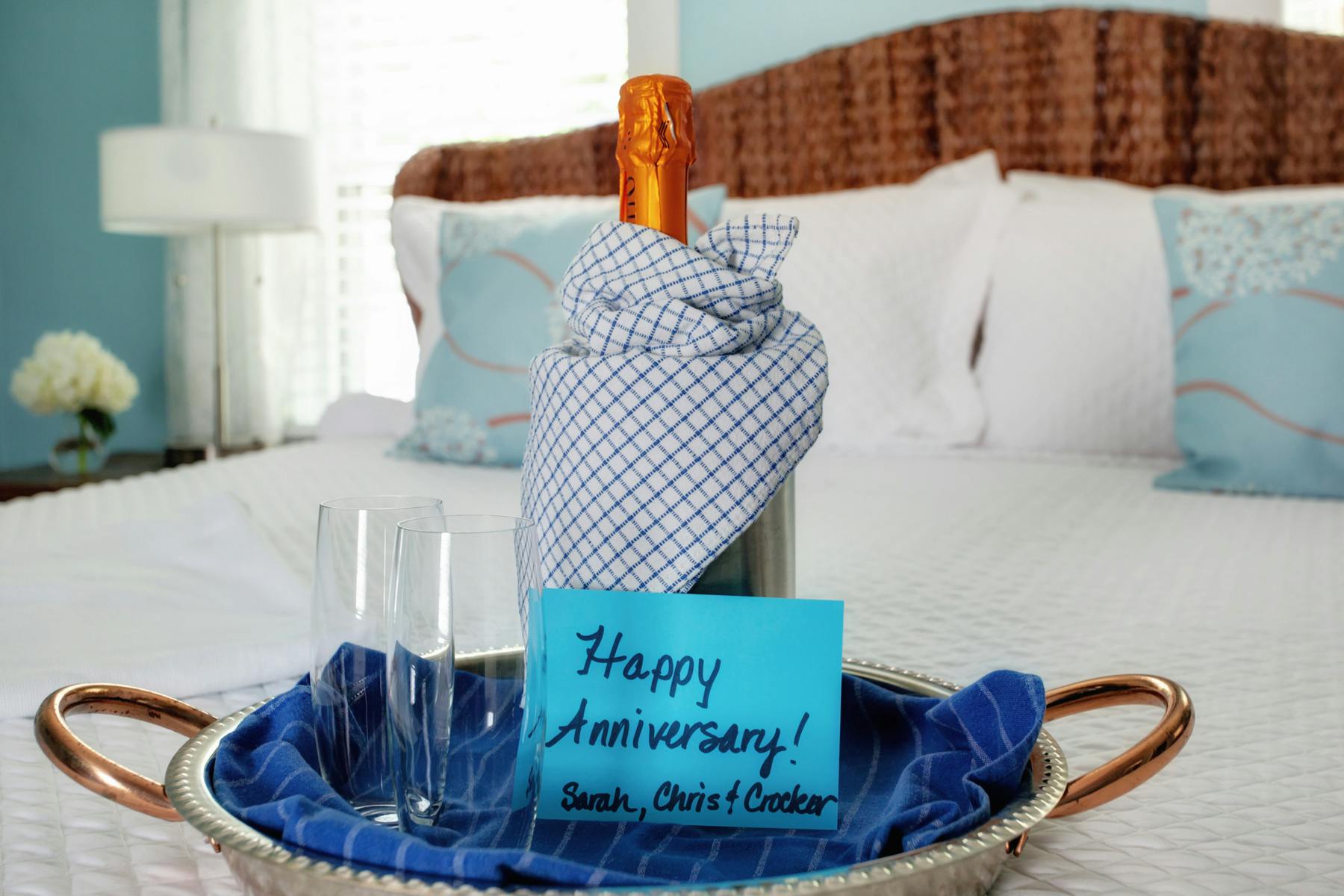 Serving tray on bed with bottle of champagne, two glasses, and card that reads "Happy Anniversary!"